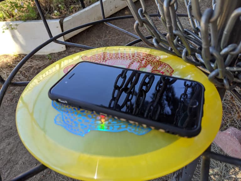 phone on disc golf disc inside of disc golf basket with chains reflection in phone face