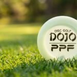 A Disc Golf Dojo PPF mini marker disc lying on short green grass on a disc golf fairway