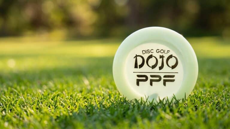 A Disc Golf Dojo PPF mini marker disc lying on short green grass on a disc golf fairway